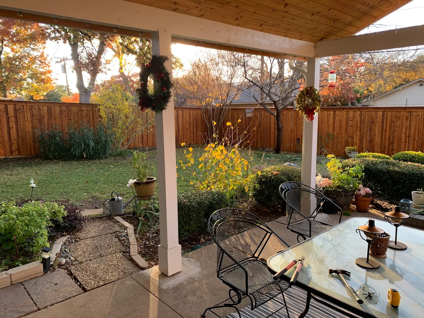 Attached patio cover on white posts over a back patio, looking out at a cedar fence and garden