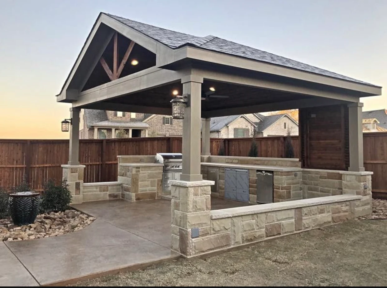 Freestanding gable patio cover on stone-wrapped columns over an outdoor kitchen and stamped concrete patio