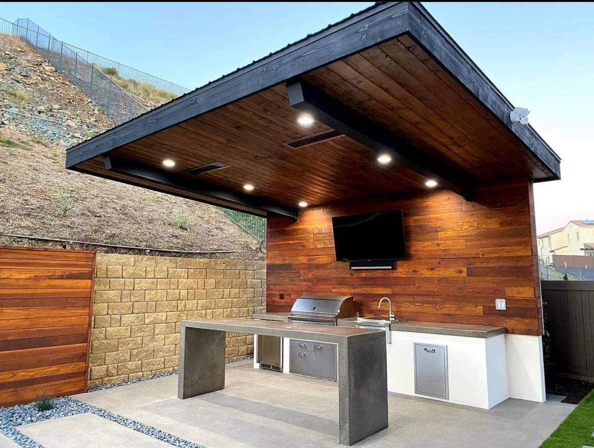 Modern shed-roof patio cover with a cedar ceiling and recessed lights over an outdoor kitchen with a grill and mounted TV